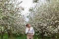Beautiful young blonde woman in white shirt posing under apple tree in blossom in Spring garden Royalty Free Stock Photo