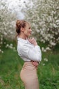 Beautiful young blonde woman in white shirt posing under apple tree in blossom in Spring garden Royalty Free Stock Photo