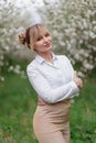 Beautiful young blonde woman in white shirt posing under apple tree in blossom in Spring garden Royalty Free Stock Photo