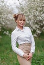 Beautiful young blonde woman in white shirt posing under apple tree in blossom in Spring garden Royalty Free Stock Photo