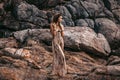 Beautiful young boho style woman on stones background at sunset