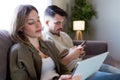 Beautiful young bored couple using their digital tablet and smartphone at home. Royalty Free Stock Photo