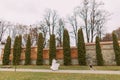 Beautiful young bride in candid gown and fur jacket on the lane at the autumn park inside fortified castle walls