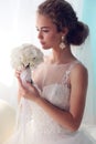 Beautiful young bride with dark curly hair in luxurious wedding dress posing at room Royalty Free Stock Photo