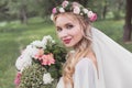 beautiful young bride in floral wreath and veil holding bouquet and smiling Royalty Free Stock Photo