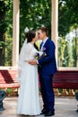Beautiful young bride and groom kissing near a wooden bench in the park. Wedding couple in love at wedd day Royalty Free Stock Photo