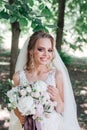 Beautiful young bride holding wedding bouquet and smiling at camera outdoor Royalty Free Stock Photo