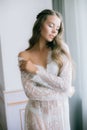 Beautiful young bride with long blond curly hair in a long white lacy dressing gown in the morning Royalty Free Stock Photo