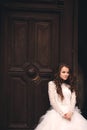 Beautiful young bride near the ancient door. Wedding portrait of a stylish woman in white long dress near old house in in a Royalty Free Stock Photo