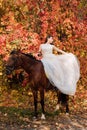 A beautiful young bride sits astride a horse. Autumn Forest Royalty Free Stock Photo