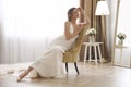 Beautiful young bride wearing elegant wedding dress sitting in armchair Royalty Free Stock Photo