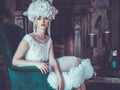 Beautiful young bride wearing white dress and wreath of flowers sits on a chair. Luxury palace. Royalty Free Stock Photo