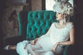 Beautiful young bride wearing white dress and wreath of flowers sits on a chair. Luxury palace. Royalty Free Stock Photo