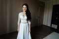 Beautiful young bride in white dress waiting for the groom indoors.