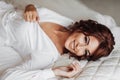Beautiful young bride in white peignoir lying on bed in hotel bedroom. Royalty Free Stock Photo