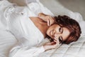 Beautiful young bride in white peignoir lying on bed in hotel bedroom. Royalty Free Stock Photo