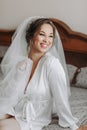 Beautiful young bride in white petticoat and tiara sitting posing on bed in her bedroom Royalty Free Stock Photo