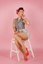 Beautiful young bright girl in retro style pin-up style, sits on a white step ladder on a pink glamorous background Royalty Free Stock Photo