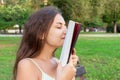 Beautiful young brownhair girl smells a fresh printed book sitting on the bench in the park