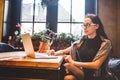 Beautiful young brunette business woman wearing glasses and sweater uses laptop to print text on keyboard. In coffee house, sittin Royalty Free Stock Photo