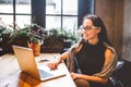 Beautiful young brunette business woman wearing glasses and sweater uses laptop to print text on keyboard. In coffee house, sittin Royalty Free Stock Photo