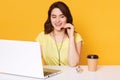 Beautiful young brunette female in headphones with microphone sits at white table with laptop, talking with client, answering Royalty Free Stock Photo