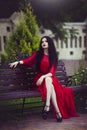 Beautiful young brunette girl in red dress is sitting on a bench. Royalty Free Stock Photo