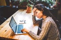 Beautiful young brunette girl in sweater working on laptop computer inside cafe at wooden table near window. Winter and Christmas Royalty Free Stock Photo