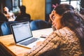 Beautiful young brunette girl in sweater working on laptop computer inside cafe at wooden table near window. Winter and Christmas Royalty Free Stock Photo