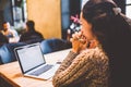 Beautiful young brunette girl in sweater working on laptop computer inside cafe at wooden table near window. Winter and Christmas Royalty Free Stock Photo