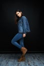 Beautiful young brunette woman in denim clothes posing against dark studio background. Royalty Free Stock Photo