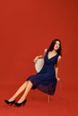 Beautiful young brunette woman in elegant blue cocktail dress and black high heels is posing for the camera sitting on Royalty Free Stock Photo