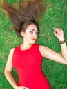 Beautiful young brunette woman lies on the grass, laying her hair, in a red dress.