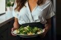 Beautiful Young Brunette Woman With Long Hair Holding Plate Of Avocado And Salad In Front Of Modern Kitchen. Generative AI