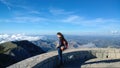 Beautiful young brunette woman with long hair standing on the edge of a cliff with a backpack at the memorial Njegos Royalty Free Stock Photo