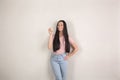 Beautiful young brunette woman with long hair is standing by the grey background holding a green apple in her hand and smiling. Royalty Free Stock Photo