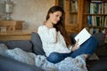 Beautiful young woman reading a book on a gray sofa. Royalty Free Stock Photo
