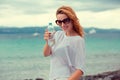 Beautiful young brunette woman in sunglasses drinking water and cooling off after running at the beach on a sea background. Royalty Free Stock Photo