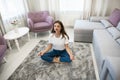 Beautiful young brunette woman wearing jeans and white t-shirt sitting on the floor in asana yoga pose in bright