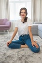 Beautiful young brunette woman wearing jeans and white t-shirt sitting on the floor in bright livingroom