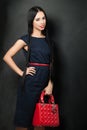 Beautiful young brunette woman wearing nice clothes holding red handbag posing on black background. Fashion photo Royalty Free Stock Photo