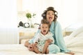 Beautiful young brunette woman and cute baby girl wearing blue bathrobes with curlers having fun on the bed in bright Royalty Free Stock Photo