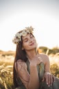 Woman in wreath of flowers and khaki dress walk in field and collect flowers. Summer sunset. Rustic style