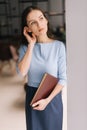 Beautiful young business woman holding file folder while standing near window in modern office room. Royalty Free Stock Photo