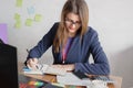 A beautiful young business woman is sitting at a desk, smiling, writing with a pencil in a notebook Royalty Free Stock Photo