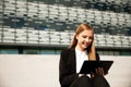 Beautiful young business woman worko on tablet on stairs in front of office building