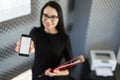 Beautiful young businesswoman in black dress and glasses hold paper folder and show phone Royalty Free Stock Photo