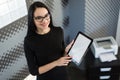 Beautiful young businesswoman in black dress and glasses hold paper folder and show tablet Royalty Free Stock Photo