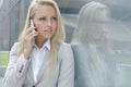 Beautiful young businesswoman conversing on cell phone while looking away by glass wall Royalty Free Stock Photo