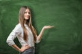 Beautiful young businesswoman holding her open palm and showing at the empty area on green chalkboard Royalty Free Stock Photo